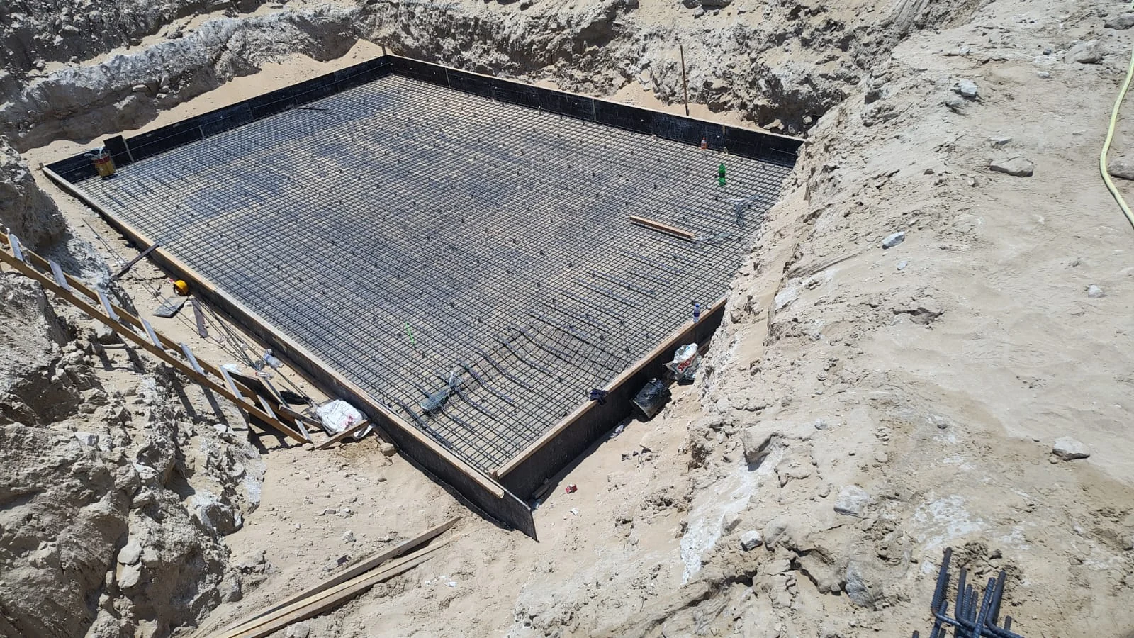 Steel reinforcement mesh laid within rectangular foundation formwork at the base of an excavation.